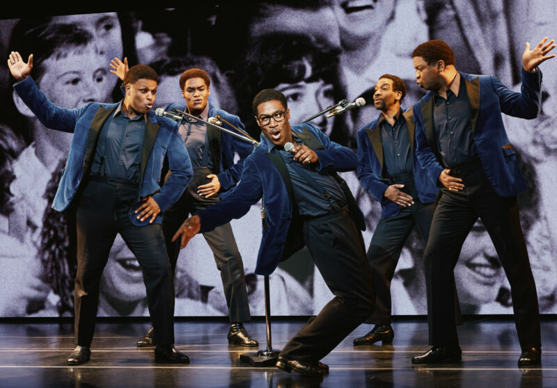 Harrell Holmes Jr., Jalen Harris, Elijah Ahmad Lewis, E. Clayton Cornelious and Michael Andreaus from the National Touring Company of Ain’t Too Proud. The Temptations are all lean back as they sing into microphones. All are wearing blue velvet suit jackets and wearing matching shirts, pants and suspenders.